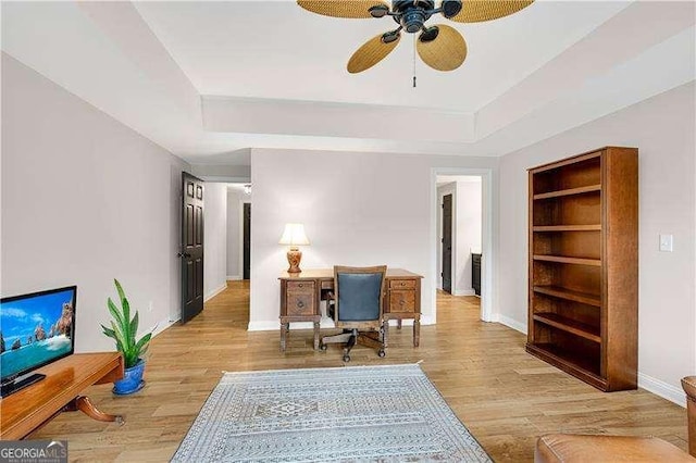 home office with a tray ceiling, ceiling fan, light hardwood / wood-style floors, and built in features