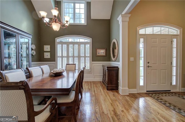 dining area featuring a high ceiling, ornate columns, an inviting chandelier, and light hardwood / wood-style flooring