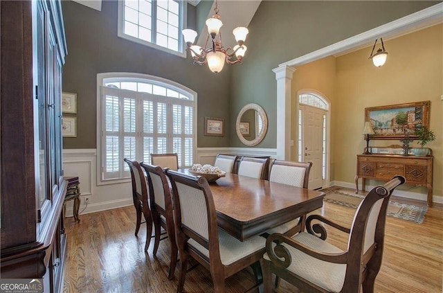 dining space with light wood-type flooring, an inviting chandelier, decorative columns, and a high ceiling