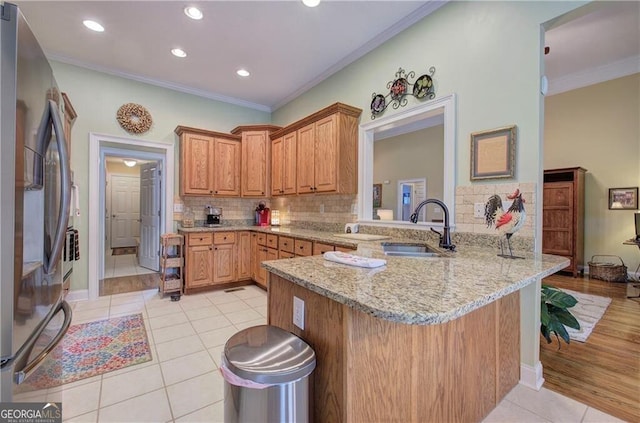 kitchen with light stone countertops, backsplash, sink, stainless steel fridge with ice dispenser, and kitchen peninsula