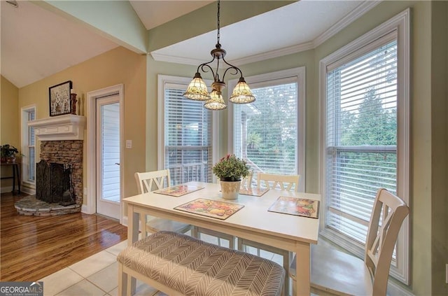 dining room featuring a healthy amount of sunlight, vaulted ceiling, a chandelier, and a stone fireplace