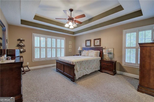 bedroom featuring a raised ceiling, light carpet, and ceiling fan