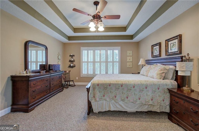 carpeted bedroom with ceiling fan and a raised ceiling