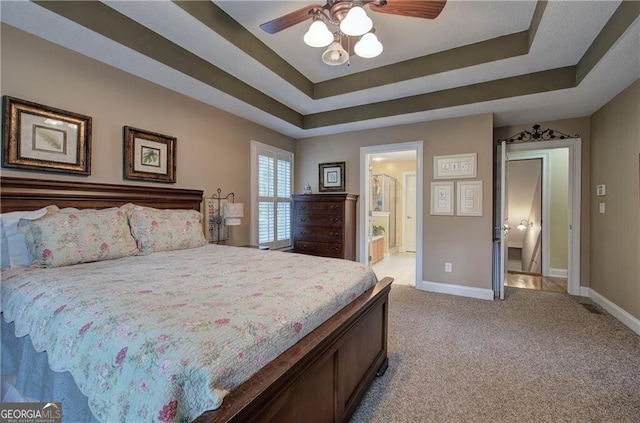 bedroom featuring a tray ceiling, ceiling fan, light carpet, and ensuite bathroom