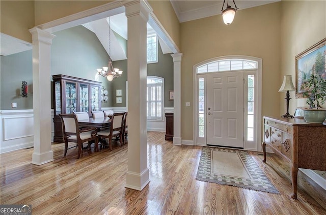 foyer entrance with light hardwood / wood-style flooring, ornate columns, a high ceiling, and a notable chandelier