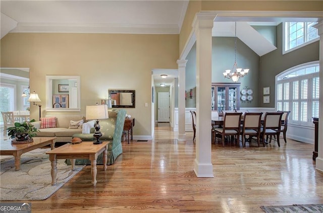 living room featuring light wood-type flooring, an inviting chandelier, a high ceiling, ornate columns, and crown molding