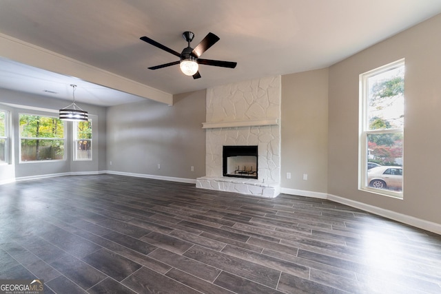 unfurnished living room with ceiling fan, beamed ceiling, dark hardwood / wood-style floors, and a stone fireplace