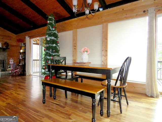 dining area featuring lofted ceiling with beams, a stone fireplace, an inviting chandelier, and wood finished floors