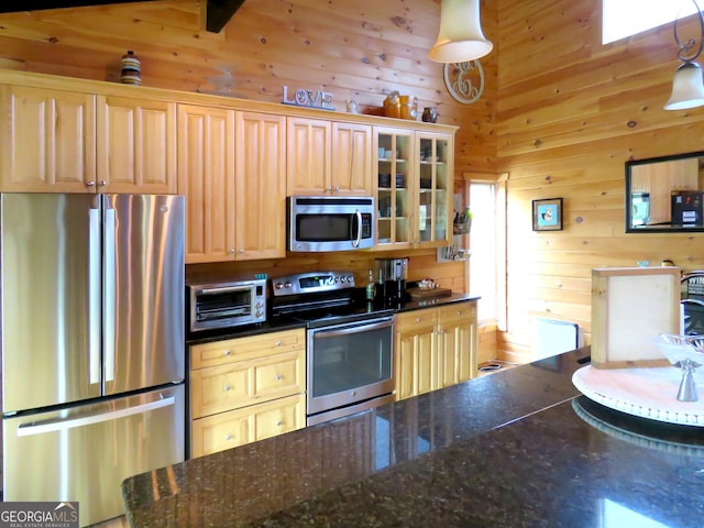 kitchen with dark countertops, appliances with stainless steel finishes, glass insert cabinets, decorative light fixtures, and wood walls