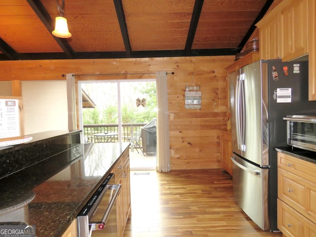 kitchen featuring lofted ceiling with beams, wooden walls, stainless steel appliances, dark stone countertops, and decorative light fixtures