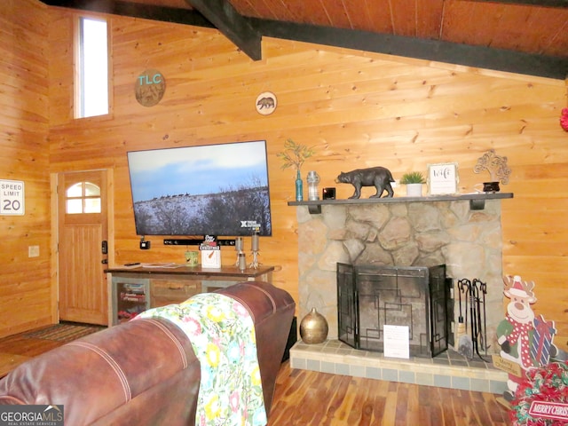 living room featuring lofted ceiling with beams, wood walls, a stone fireplace, wood finished floors, and wooden ceiling