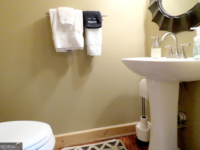 half bath with baseboards, toilet, and wood finished floors