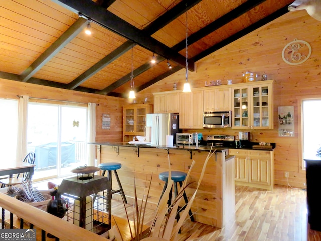 kitchen featuring dark countertops, glass insert cabinets, hanging light fixtures, stainless steel appliances, and wood walls