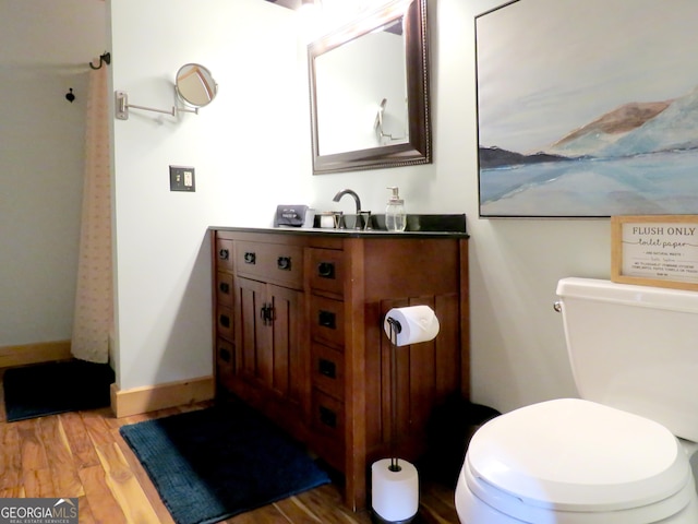 bathroom featuring toilet, baseboards, wood finished floors, and vanity