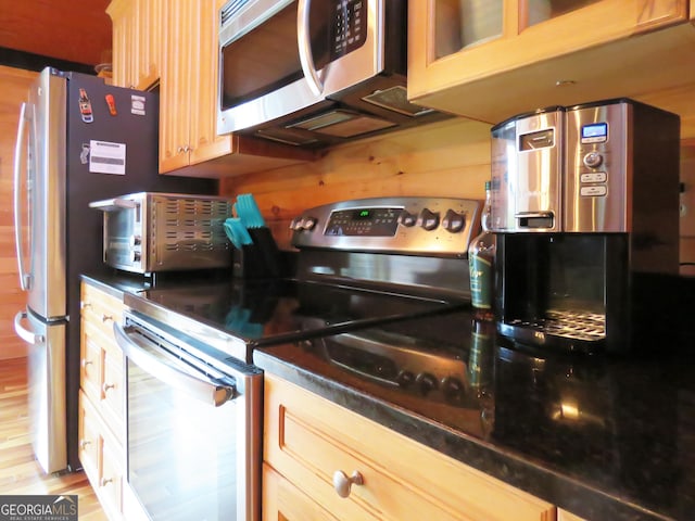 kitchen with dark countertops, appliances with stainless steel finishes, glass insert cabinets, and light brown cabinetry