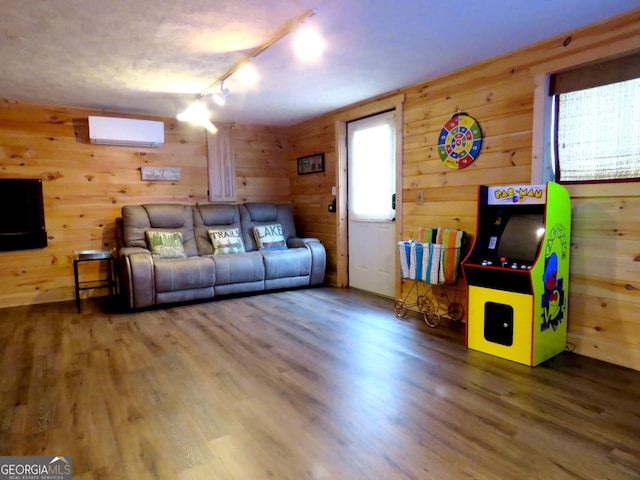 living area with an AC wall unit, track lighting, wood finished floors, and wooden walls