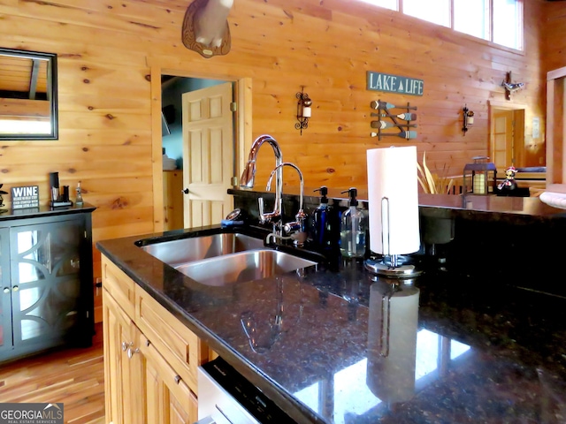 kitchen featuring light brown cabinetry, dark stone counters, a sink, wooden walls, and light wood-type flooring