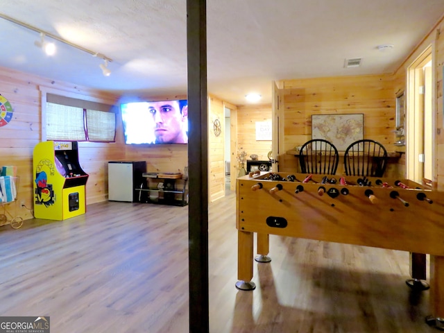 game room featuring rail lighting, wood finished floors, visible vents, and wooden walls