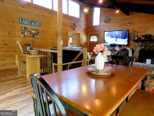 dining space featuring wood walls, a fireplace, high vaulted ceiling, and light wood finished floors