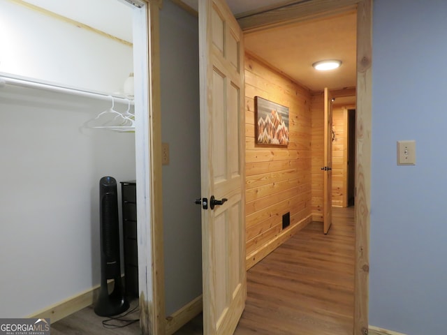 hall featuring light wood-style flooring, wooden walls, and baseboards