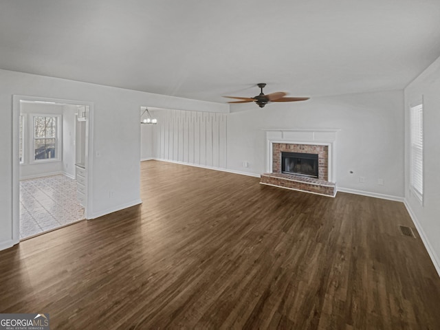 unfurnished living room featuring ceiling fan with notable chandelier, dark hardwood / wood-style flooring, and a fireplace