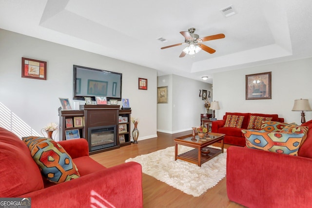 living room featuring ceiling fan, hardwood / wood-style flooring, and a tray ceiling