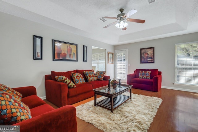 living room with hardwood / wood-style flooring, ceiling fan, a raised ceiling, and a textured ceiling