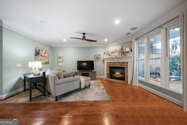 living room featuring hardwood / wood-style floors, ceiling fan, crown molding, and a fireplace