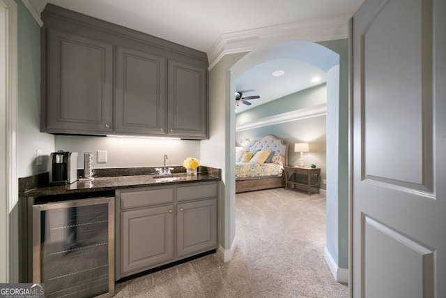 bar with sink, gray cabinets, ceiling fan, light carpet, and beverage cooler