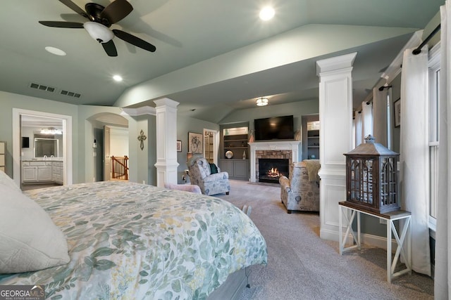 carpeted bedroom with a fireplace, ornate columns, and lofted ceiling