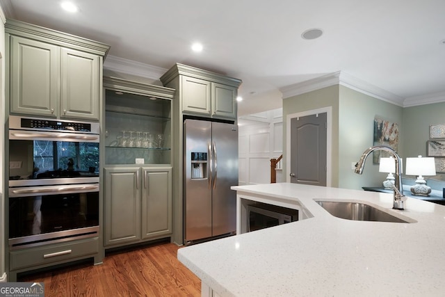 kitchen with wood-type flooring, sink, light stone counters, crown molding, and stainless steel appliances