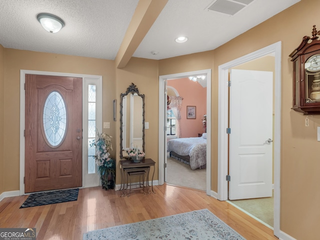 foyer featuring light wood-type flooring, baseboards, visible vents, and a textured ceiling