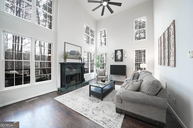 living room with dark wood-style floors, visible vents, a premium fireplace, ornamental molding, and baseboards