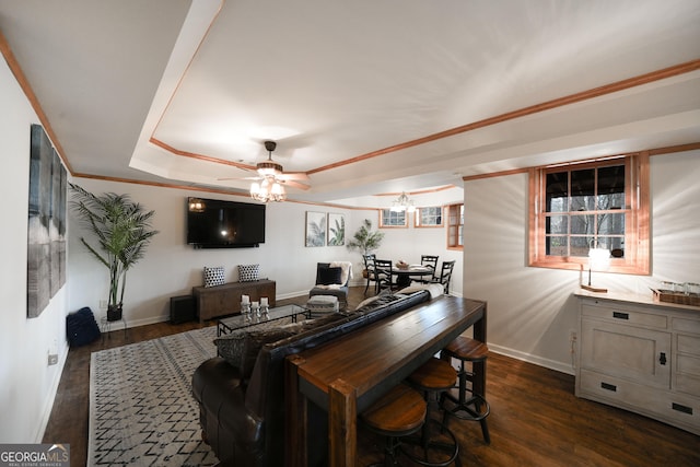 living area with ceiling fan with notable chandelier, baseboards, ornamental molding, dark wood-style floors, and a tray ceiling