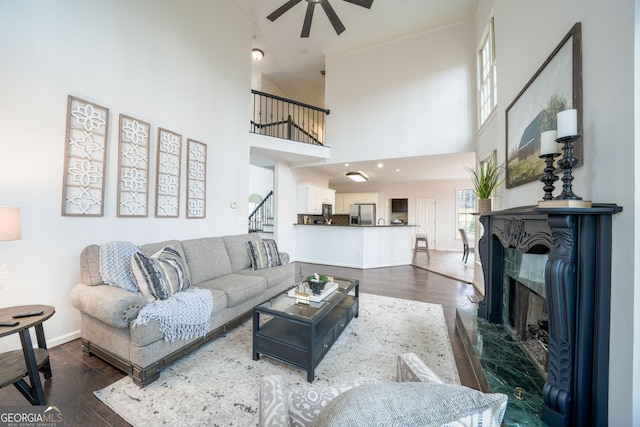 living area featuring dark wood-style flooring, a high end fireplace, ceiling fan, baseboards, and stairs