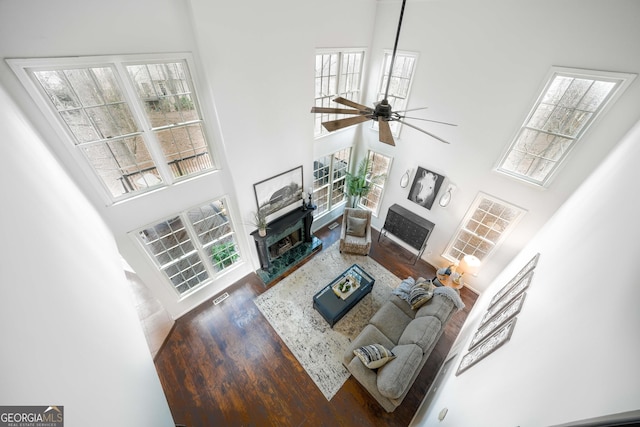 living room featuring ceiling fan, a fireplace, a high ceiling, and dark wood finished floors