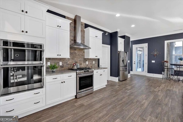 kitchen featuring appliances with stainless steel finishes, wall chimney exhaust hood, light stone countertops, crown molding, and white cabinetry