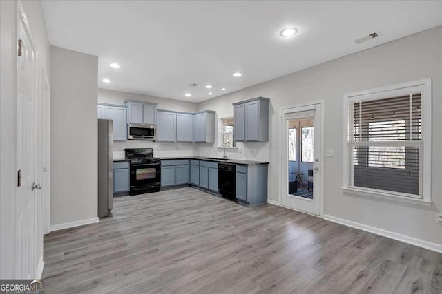 kitchen featuring visible vents, a sink, light wood finished floors, and black appliances