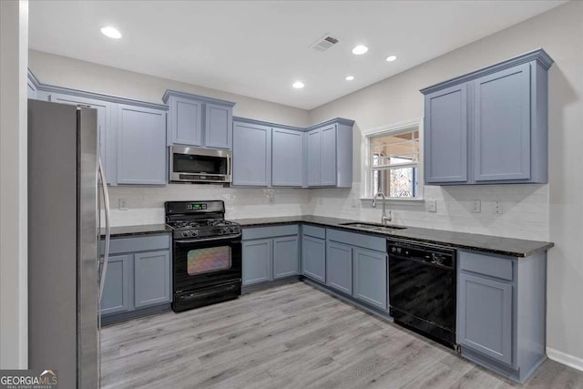 kitchen featuring light wood-style flooring, a sink, visible vents, backsplash, and black appliances