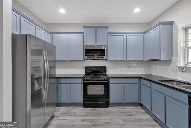 kitchen featuring decorative backsplash, dark stone counters, light wood-style flooring, appliances with stainless steel finishes, and a sink