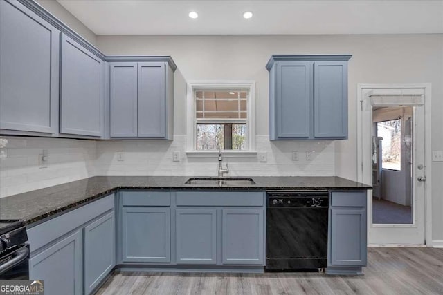 kitchen with dark stone counters, black dishwasher, a healthy amount of sunlight, and a sink