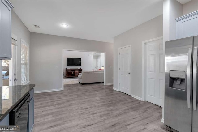 kitchen featuring dark stone counters, baseboards, light wood-style flooring, and stainless steel fridge with ice dispenser