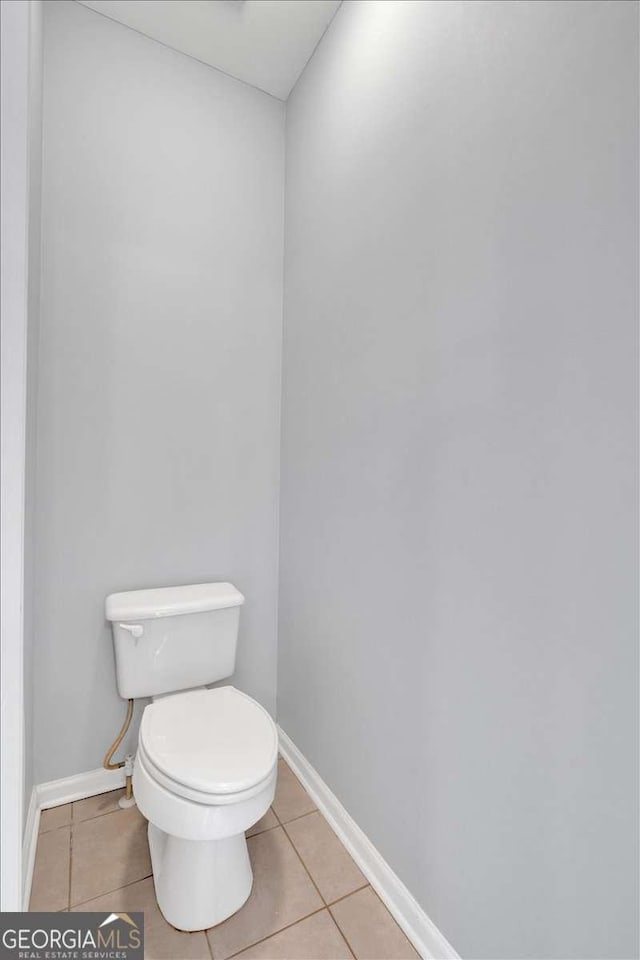 half bathroom with baseboards, toilet, and tile patterned floors