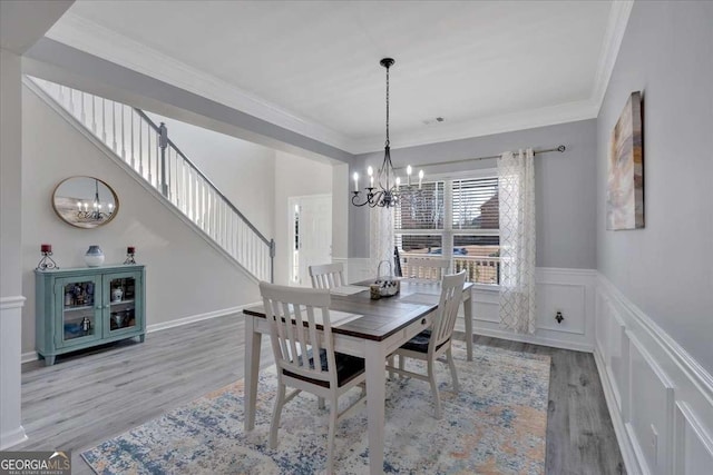 dining space featuring a wainscoted wall, ornamental molding, wood finished floors, and a notable chandelier