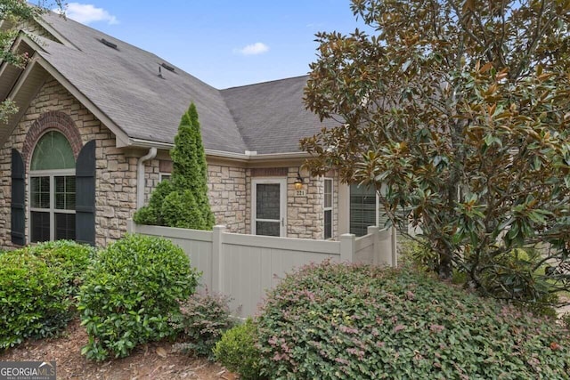 view of home's exterior with stone siding, a shingled roof, and fence