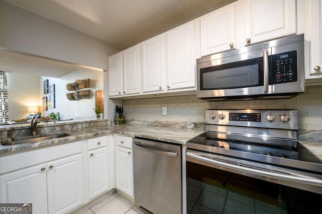 kitchen with appliances with stainless steel finishes, sink, white cabinetry, and light stone countertops