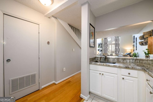 kitchen featuring light wood-type flooring, white cabinetry, sink, and a textured ceiling