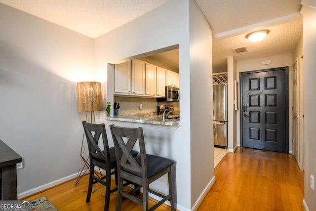 kitchen with appliances with stainless steel finishes, light hardwood / wood-style flooring, backsplash, sink, and kitchen peninsula