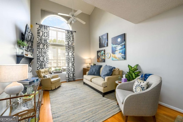 living room featuring hardwood / wood-style flooring, ceiling fan, high vaulted ceiling, and a textured ceiling