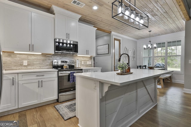 kitchen with a center island with sink, appliances with stainless steel finishes, white cabinets, and decorative light fixtures